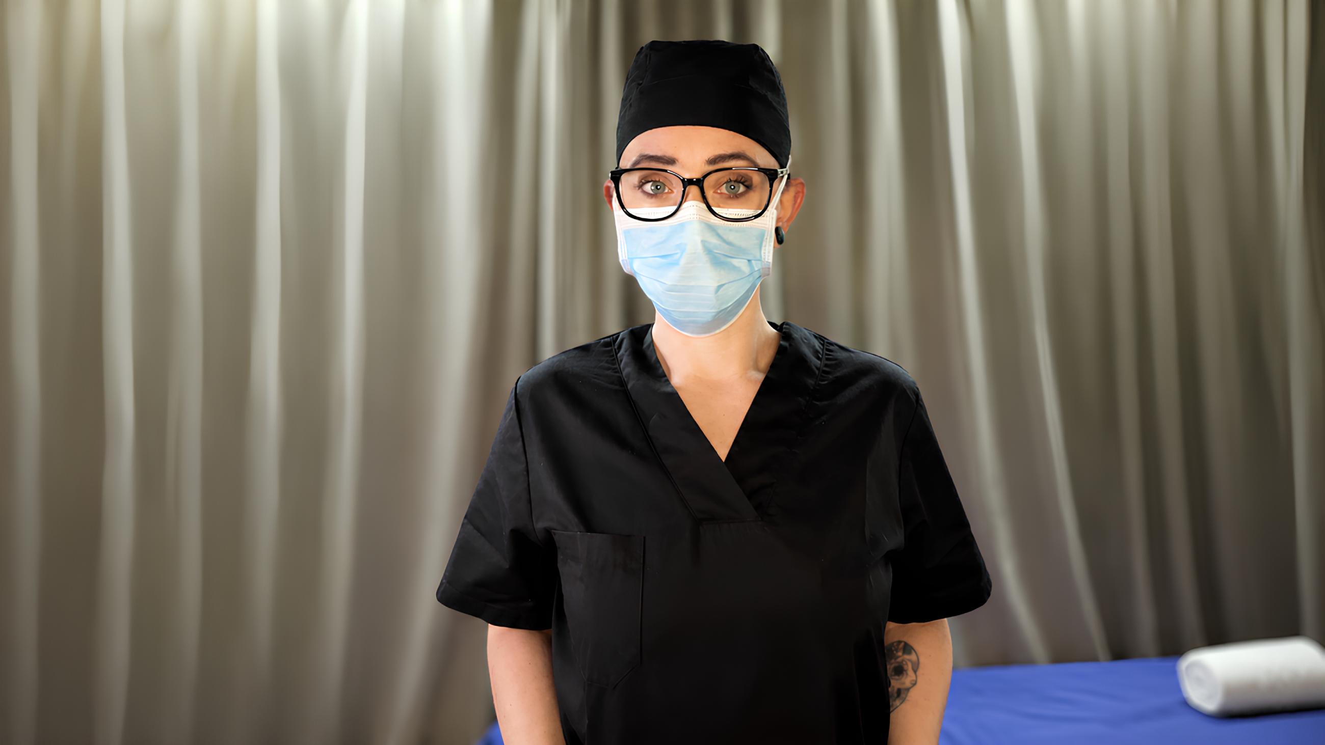 Miss Nena wearing black scrubs in a medical BDSM session reflecting on past Miss Nena drugs struggles